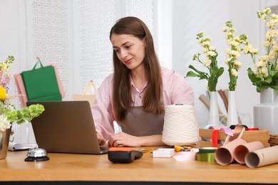 Photo of Professional florist working with laptop at wooden table in shop
