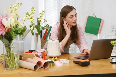 Photo of Professional florist working with laptop at wooden table in shop