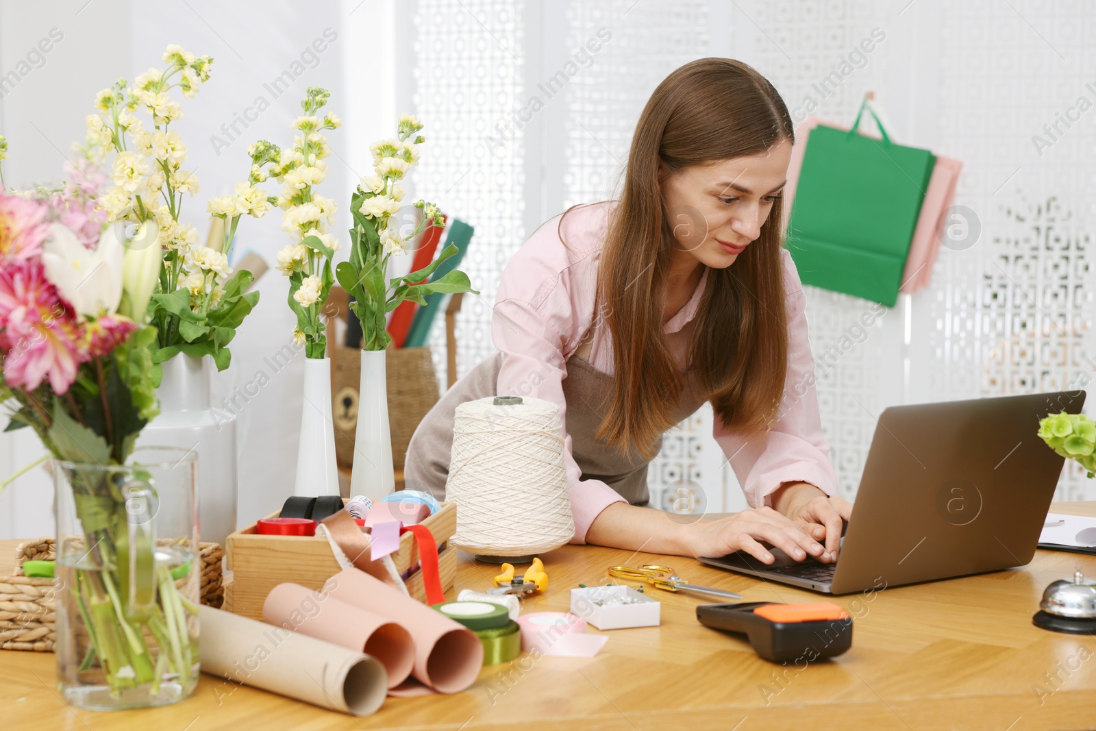 Professional florist working with laptop at wooden table in shop Photo of Professional florist working with laptop at wooden table in shop