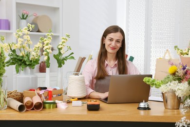 Photo of Professional florist working with laptop at wooden table in shop