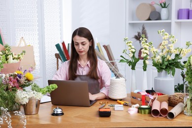 Photo of Professional florist working with laptop at wooden table in shop