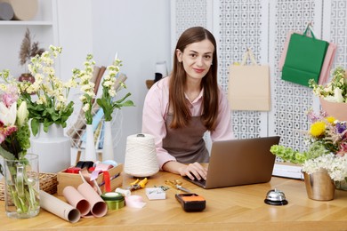 Photo of Professional florist working with laptop at wooden table in shop