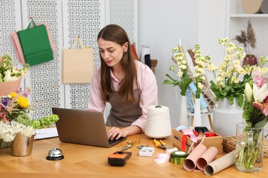 Photo of Professional florist working with laptop at wooden table in shop