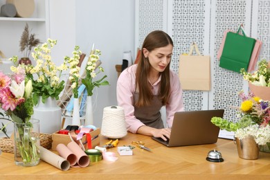 Photo of Professional florist working with laptop at wooden table in shop