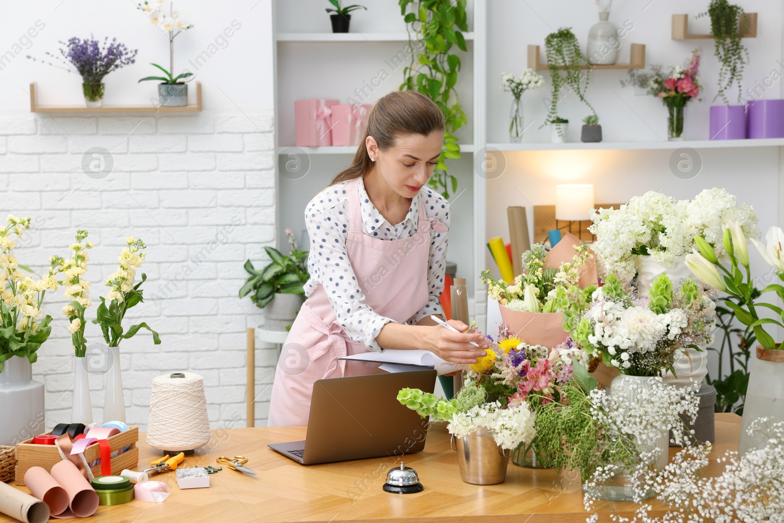 Professional florist working with laptop at wooden table in shop Photo of Professional florist working with laptop at wooden table in shop
