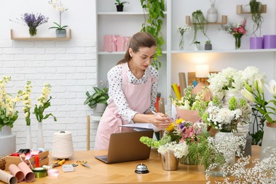 Photo of Professional florist working with laptop at wooden table in shop
