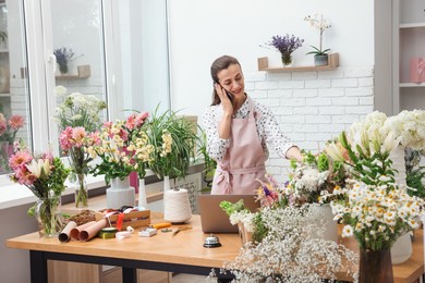 Photo of Professional florist talking on smartphone while working in shop