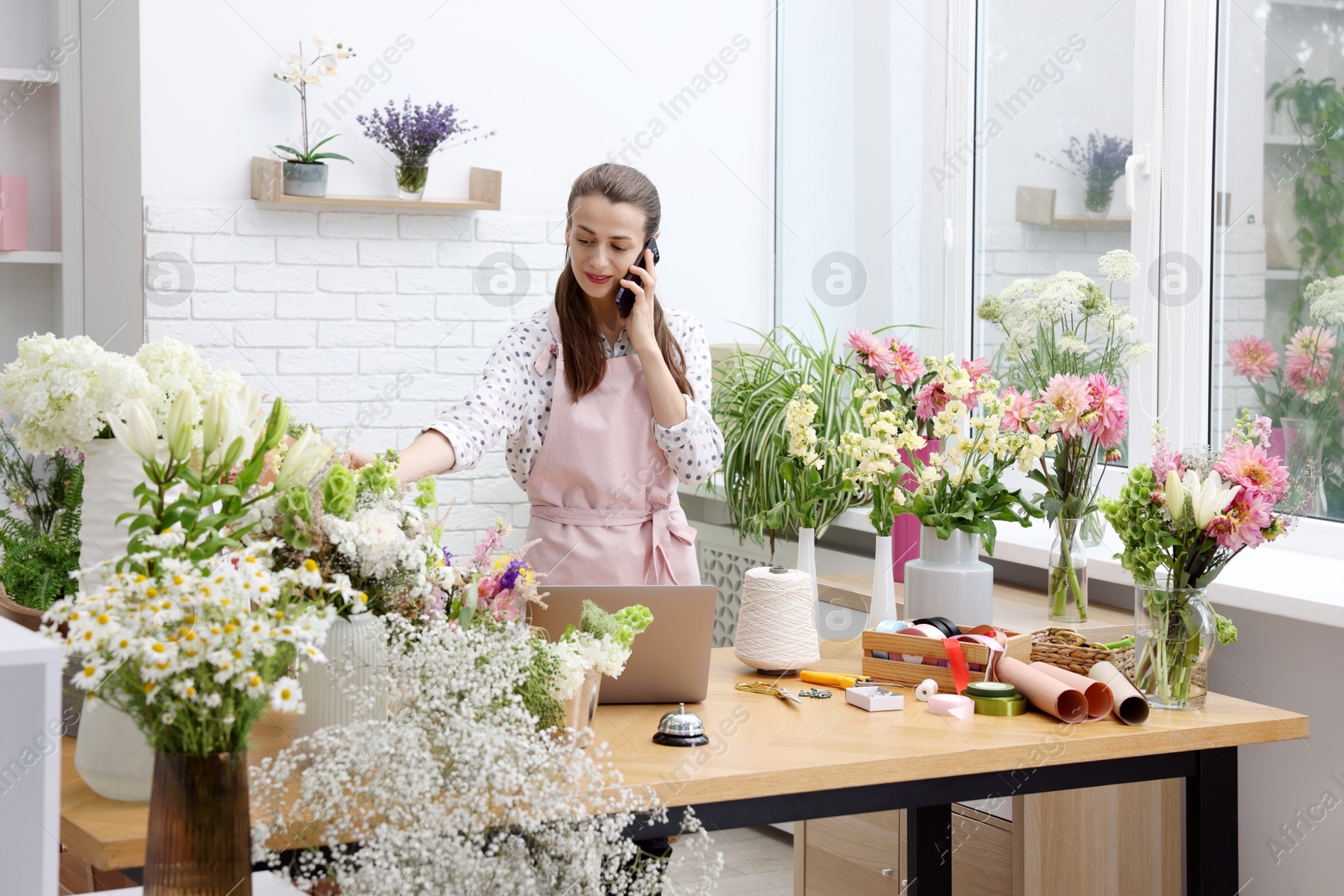 Professional florist talking on smartphone while working in shop Photo of Professional florist talking on smartphone while working in shop