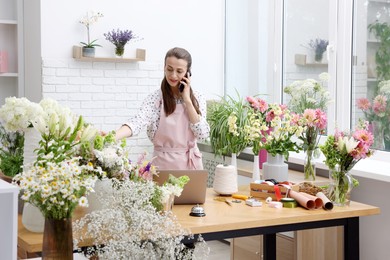 Photo of Professional florist talking on smartphone while working in shop