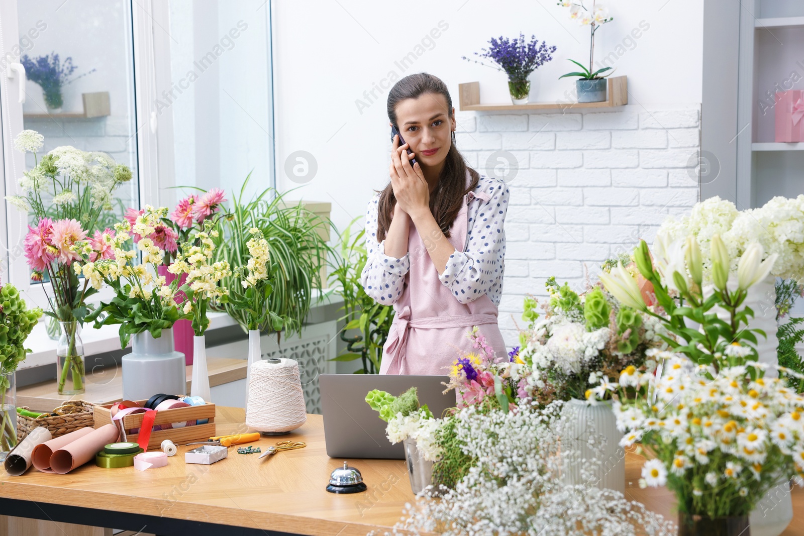 Professional florist talking on smartphone while working in shop Photo of Professional florist talking on smartphone while working in shop