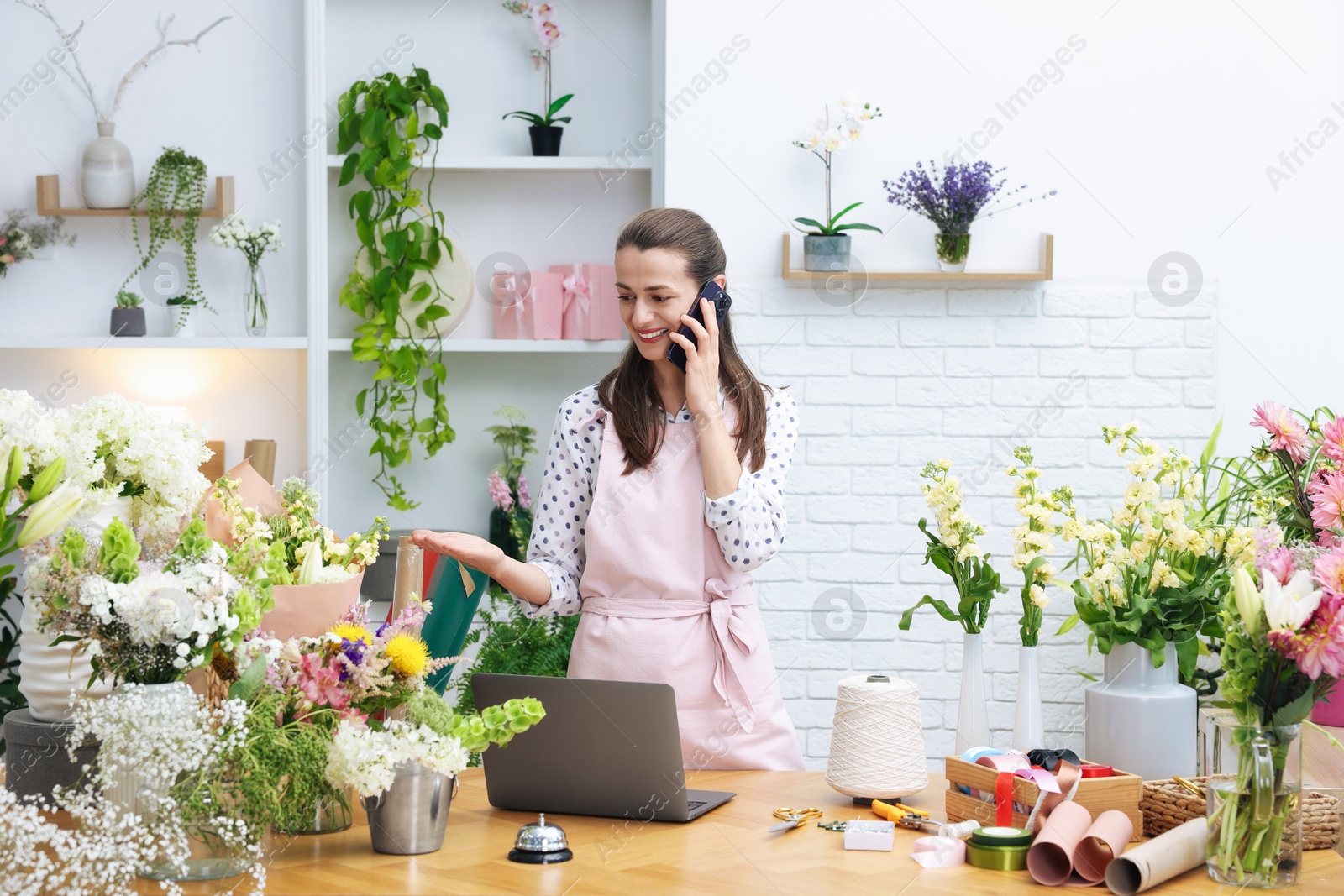 Professional florist talking on smartphone while working in shop Photo of Professional florist talking on smartphone while working in shop