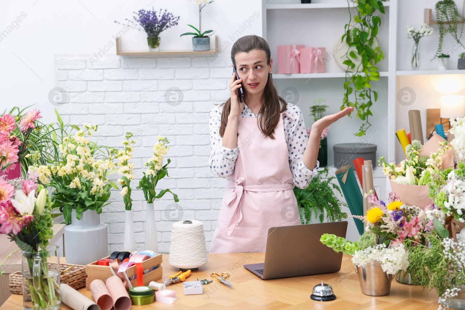 Professional florist talking on smartphone while working in shop Photo of Professional florist talking on smartphone while working in shop