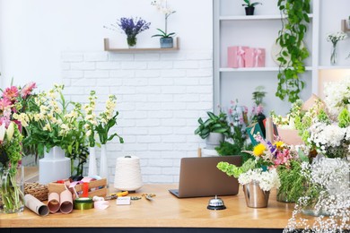 Photo of Beautiful flowers, laptop, scissors, ribbons and other tools on wooden table in florist's shop