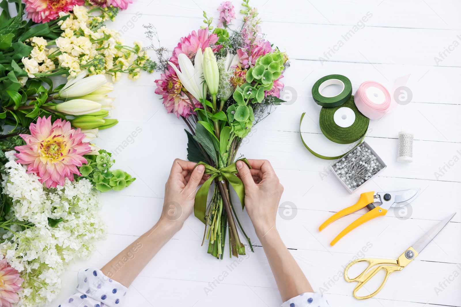 Photo of Florist making bouquet of flowers at white wooden table, top view