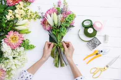 Photo of Florist making bouquet of flowers at white wooden table, top view