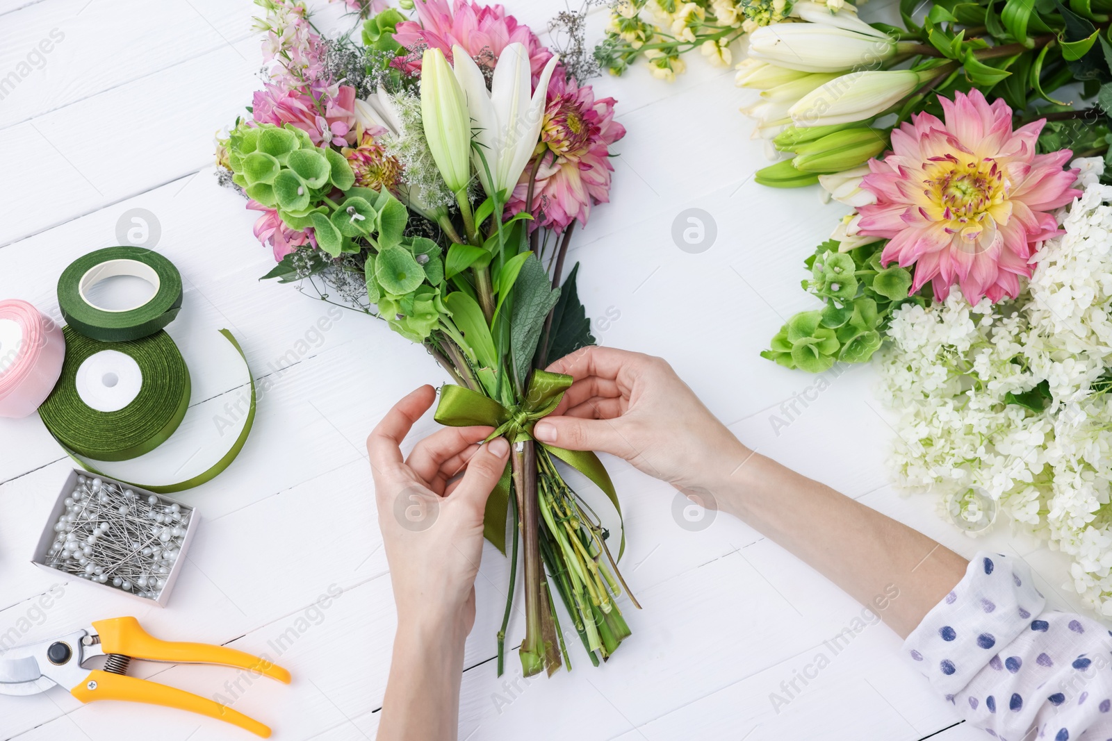 Photo of Florist making bouquet of flowers at white wooden table, top view