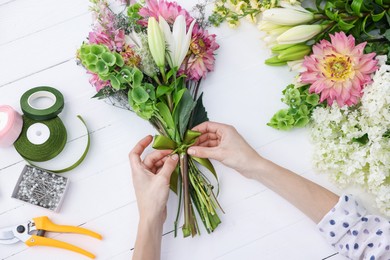 Photo of Florist making bouquet of flowers at white wooden table, top view