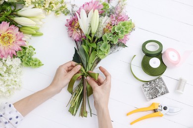 Photo of Florist making bouquet of flowers at white wooden table, top view