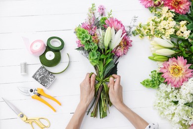 Photo of Florist making bouquet of flowers at white wooden table, top view
