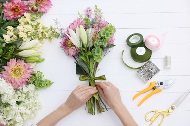 Photo of Florist making bouquet of flowers at white wooden table, top view