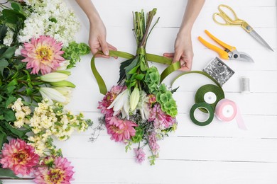 Photo of Florist making bouquet of flowers at white wooden table, top view