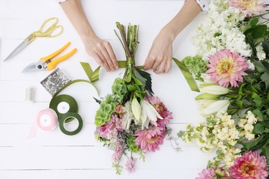 Photo of Florist making bouquet of flowers at white wooden table, top view