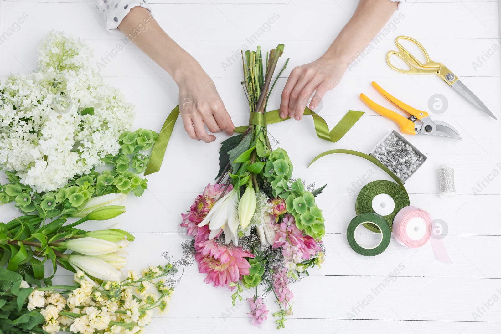 Photo of Florist making bouquet of flowers at white wooden table, top view