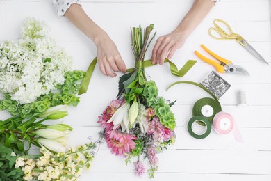 Photo of Florist making bouquet of flowers at white wooden table, top view