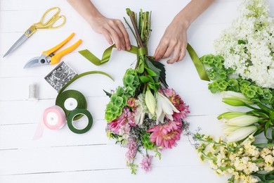 Photo of Florist making bouquet of flowers at white wooden table, top view