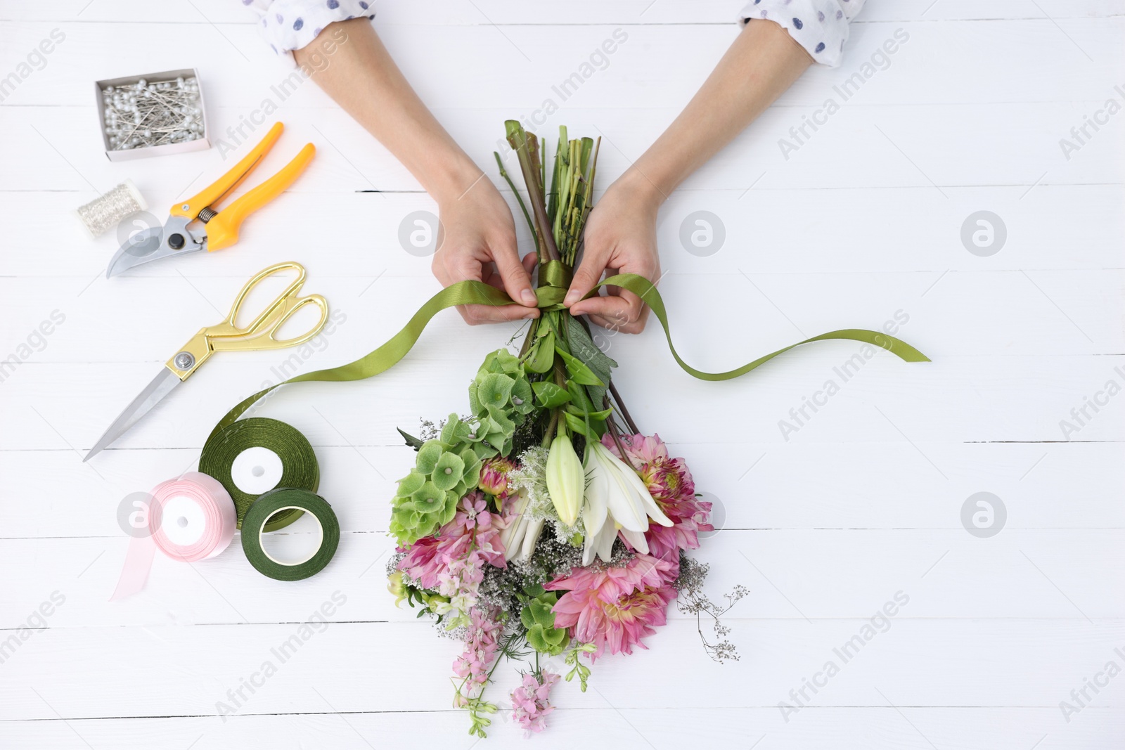 Photo of Florist making bouquet of flowers at white wooden table, top view