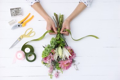 Photo of Florist making bouquet of flowers at white wooden table, top view