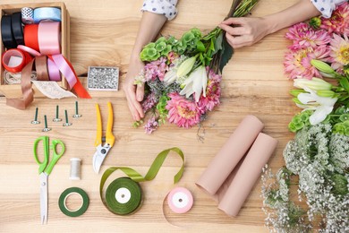 Photo of Florist making bouquet of flowers at wooden table, top view