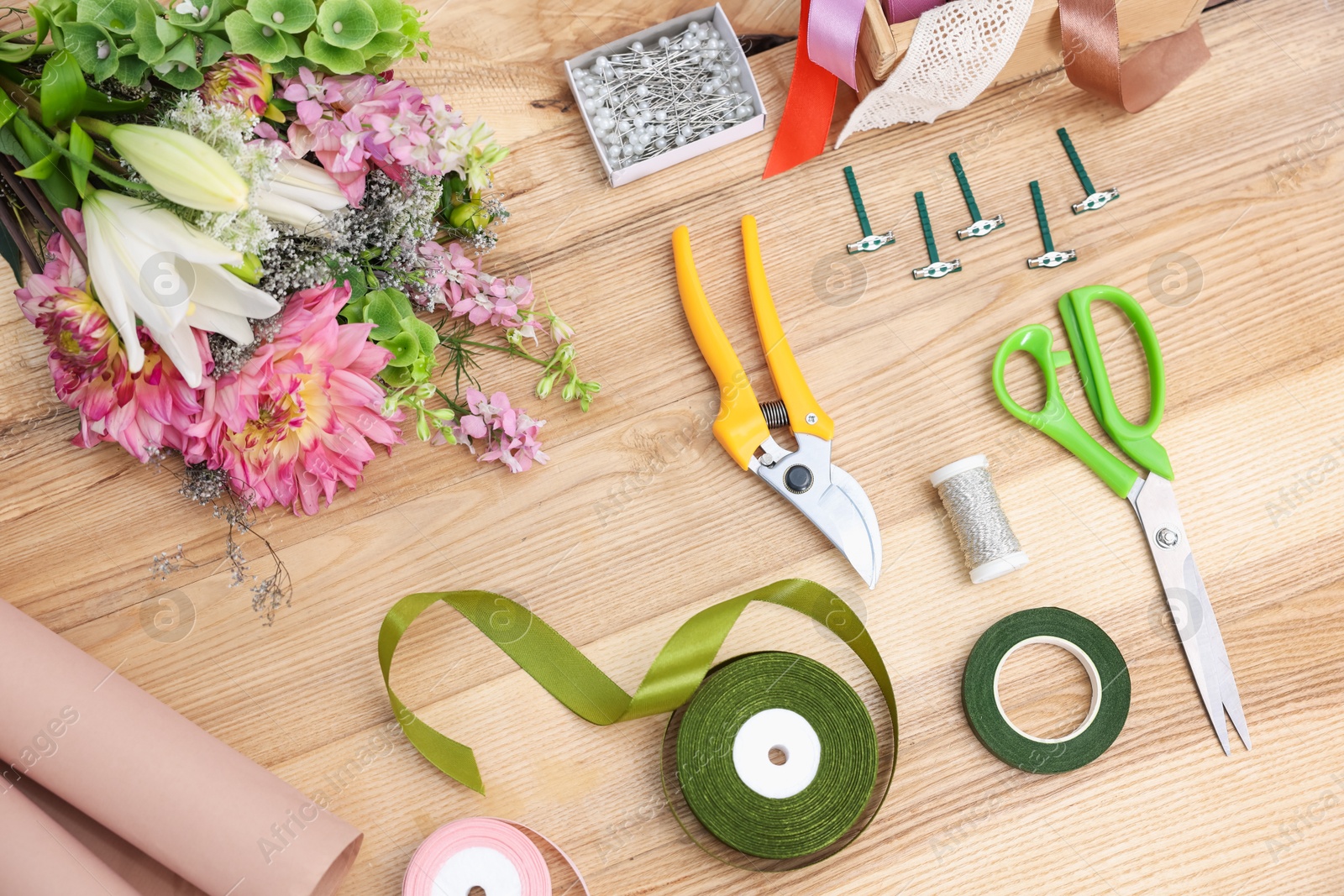 Photo of Florist. Bouquet of flowers, secateurs, scissors and ribbons on wooden table, top view