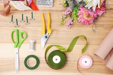 Photo of Florist. Bouquet of flowers, secateurs, scissors and ribbons on wooden table, top view