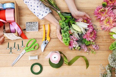 Photo of Florist making bouquet of flowers at wooden table, top view