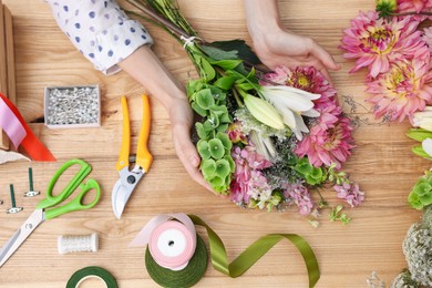 Photo of Florist making bouquet of flowers at wooden table, top view