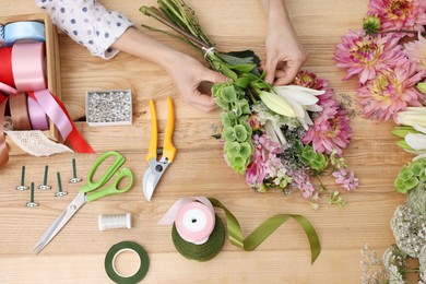 Photo of Florist making bouquet of flowers at wooden table, top view