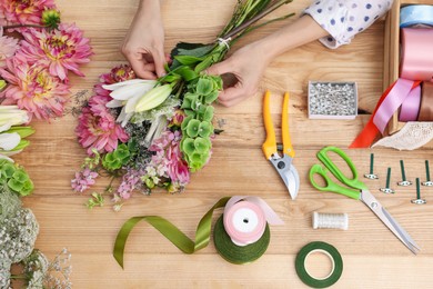 Photo of Florist making bouquet of flowers at wooden table, top view