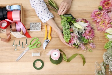 Photo of Florist making bouquet of flowers at wooden table, top view