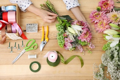 Photo of Florist making bouquet of flowers at wooden table, top view