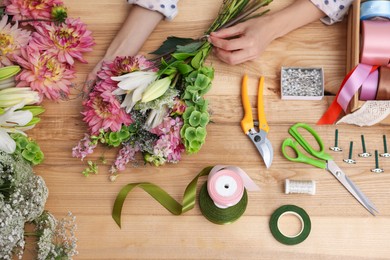 Photo of Florist making bouquet of flowers at wooden table, top view