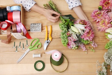 Photo of Florist making bouquet of flowers at wooden table, top view