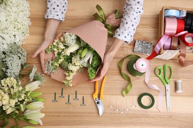 Photo of Florist making bouquet of flowers at wooden table, top view