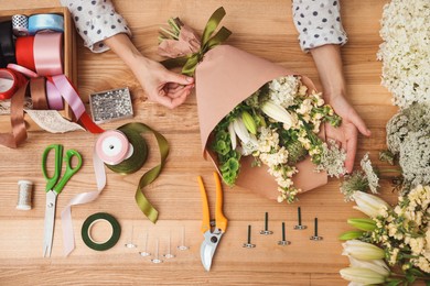 Photo of Florist making bouquet of flowers at wooden table, top view