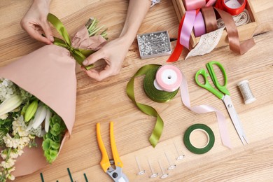 Photo of Florist making bouquet of flowers at wooden table, top view