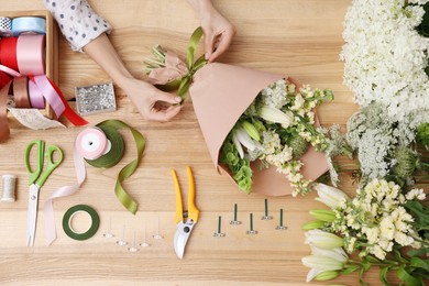 Photo of Florist making bouquet of flowers at wooden table, top view
