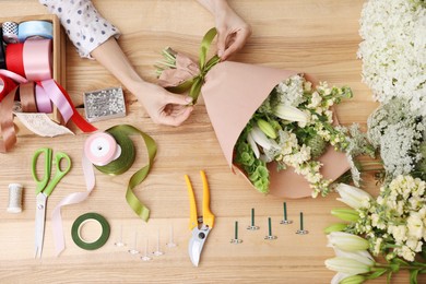 Photo of Florist making bouquet of flowers at wooden table, top view
