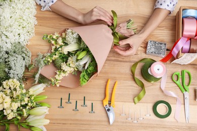 Photo of Florist making bouquet of flowers at wooden table, top view