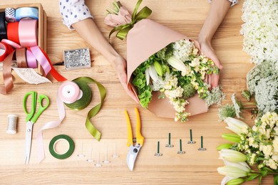 Photo of Florist making bouquet of flowers at wooden table, top view