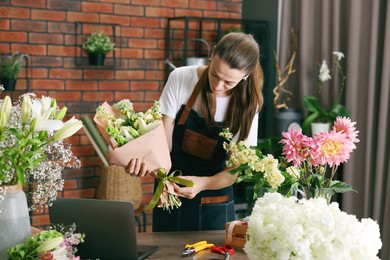 Photo of Professional florist making bouquet of flowers at wooden table in shop